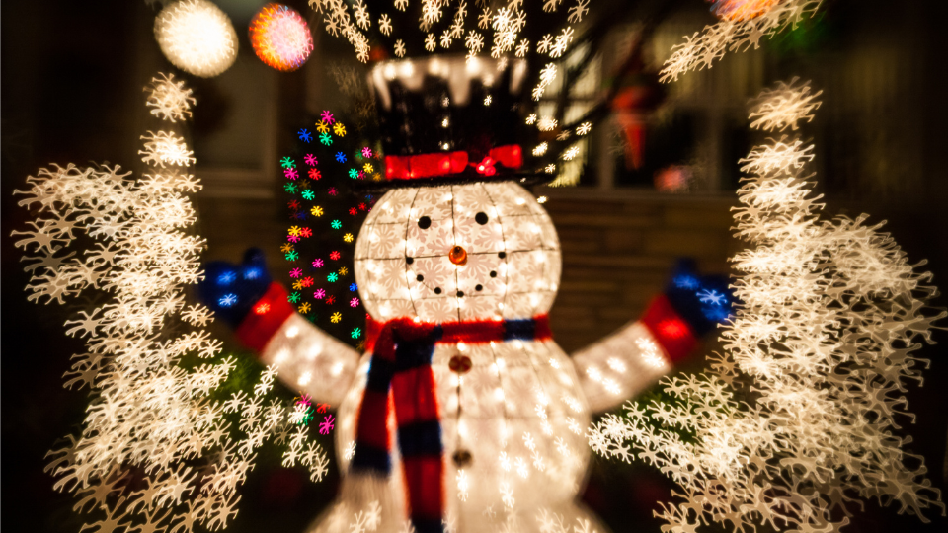 A festive snowman decoration surrounded by colorful holiday lights at night.