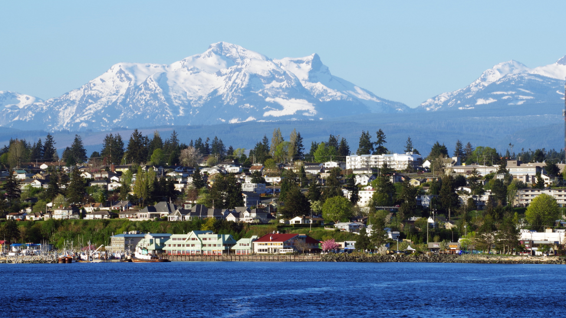 View of Campbell River, from the ocean, with the town’s shoreline in the foreground and forested mountains rising in the background.