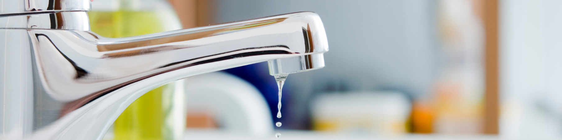A close-up of a water tap leaking, with a droplet of water falling from the spout.