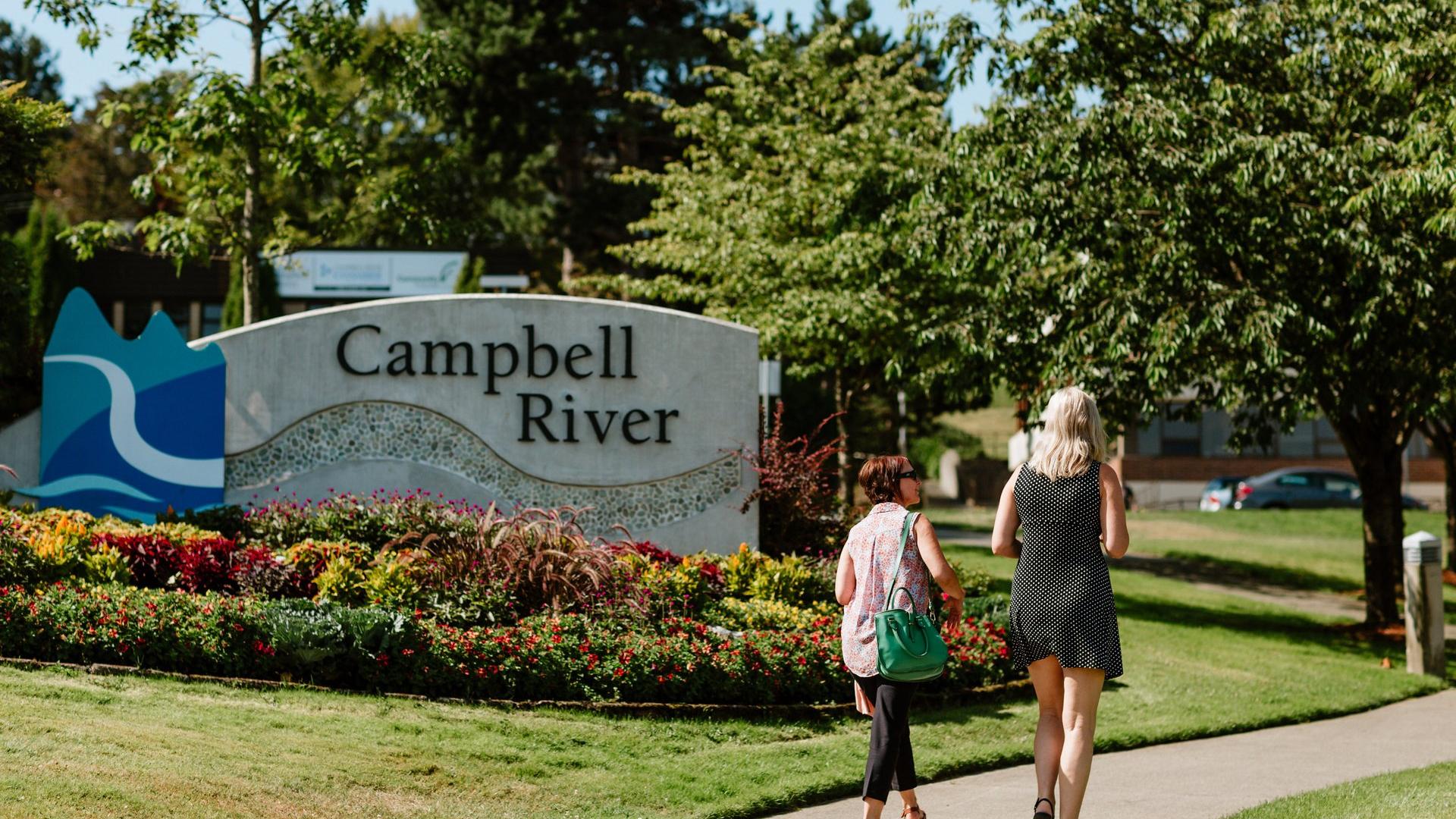 Two individuals walking along a pathway leading to City Hall, passing a sign that reads 'City Hall'