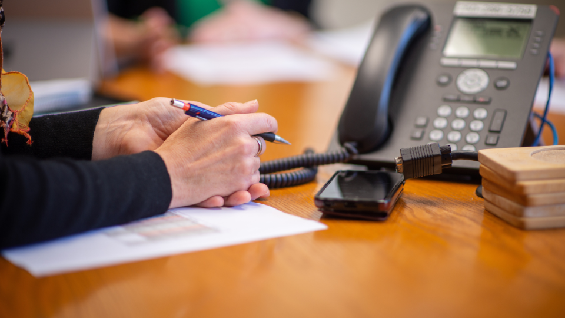 Person writing notes at a desk with a telephone nearby.