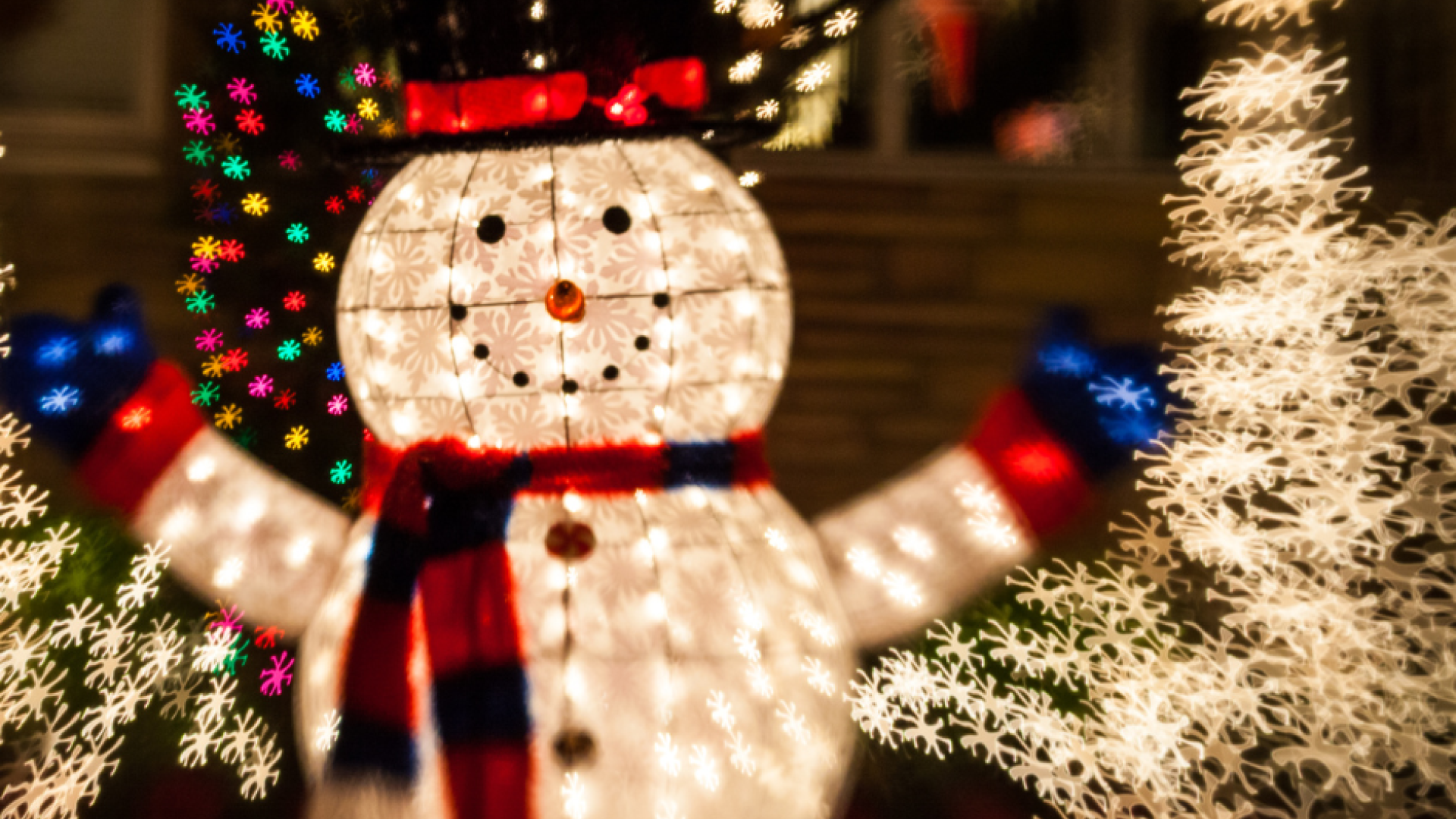 A light-up snowman decoration glowing warmly at night, surrounded by festive holiday ornaments and illuminated winter décor.