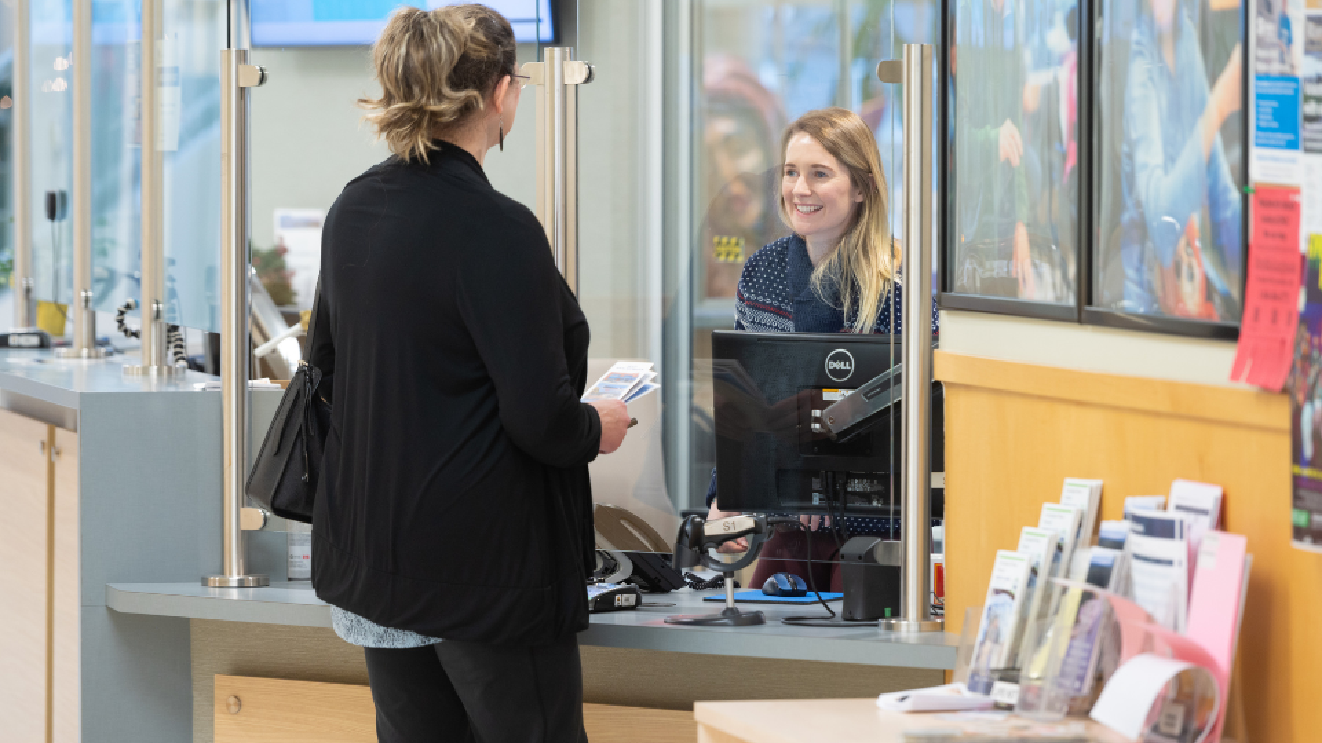 People standing at the Community Centre reception counter, smiling and engaging in friendly conversation with the staff.