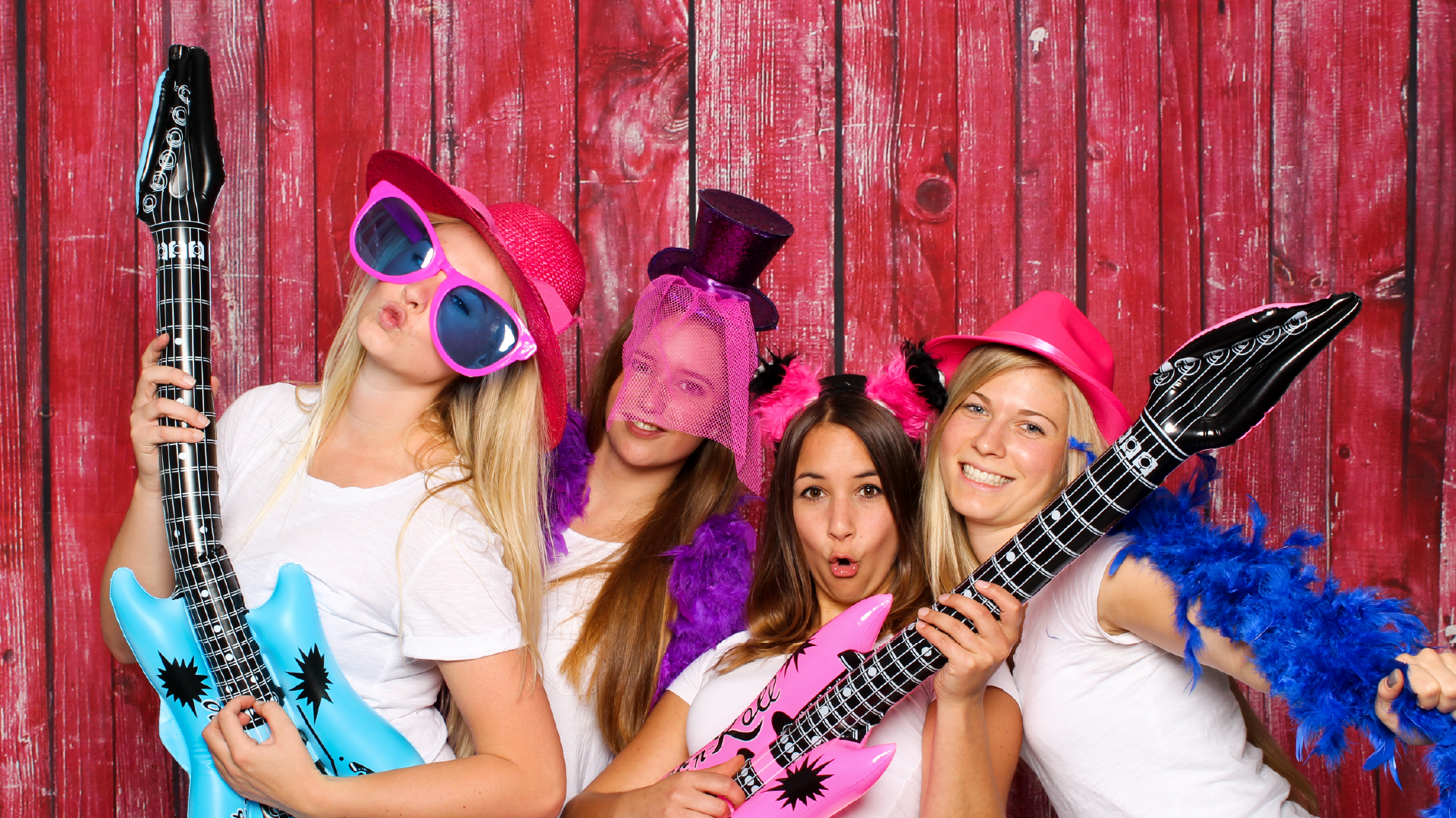Three youth in a photo booth with large sunglasses and blow up guitars having fun and laughing.