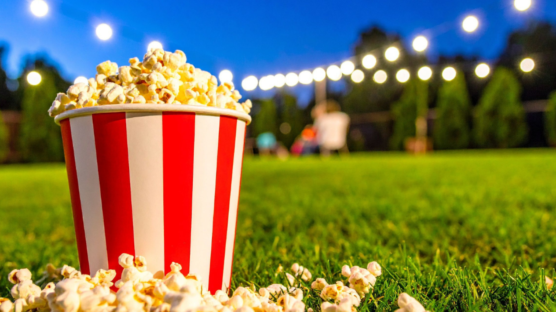 popcorn overflowing with popcorn outside under a dark sky with lights in the background.