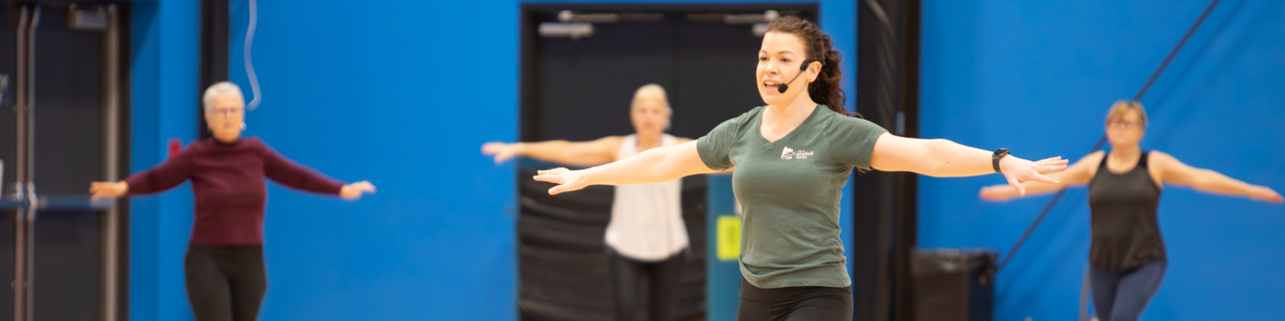 Instructor and participants in fitness class with arms pointing out to their sides