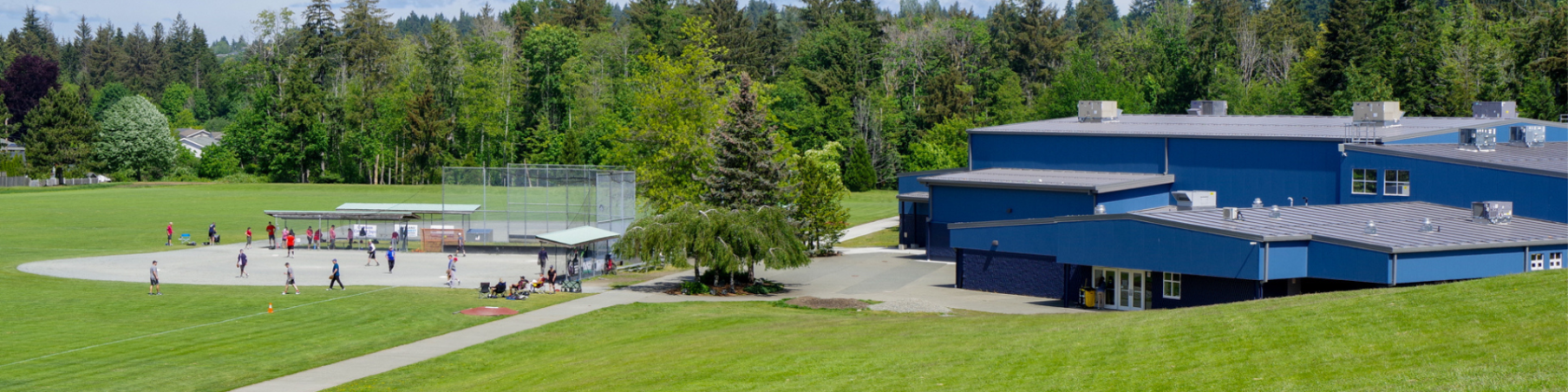 The Sportsplex is on the right with a baseball diamond and players in the background surrounded by grassy fields and tall trees