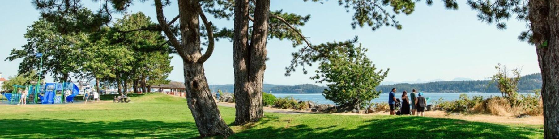 Robert V. Ostler Park (Foreshore Park) with a playground in the background and several people walking along the seawalk.