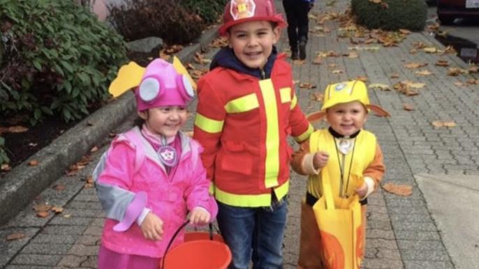 Three children downtown Campbell River in Halloween costumes laughing together.