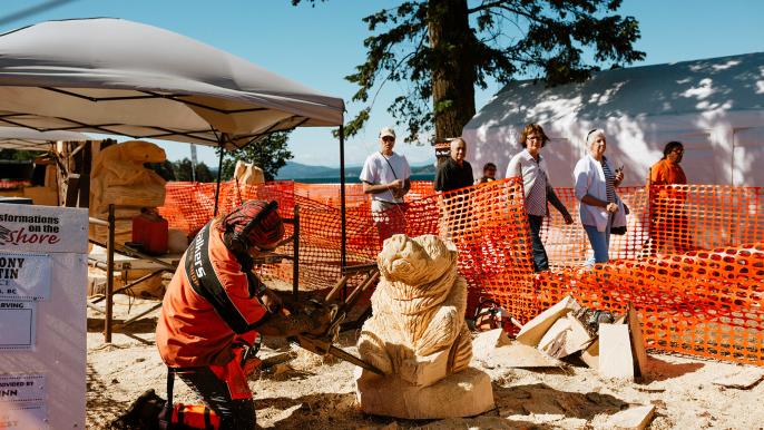 Artist with chainsaw carving a sculpture with people watching in the background