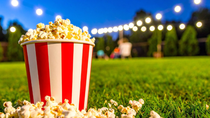 popcorn overflowing with popcorn outside under a dark sky with lights in the background.