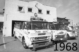 Black and white photo of fire trucks parked in front of a fire station.