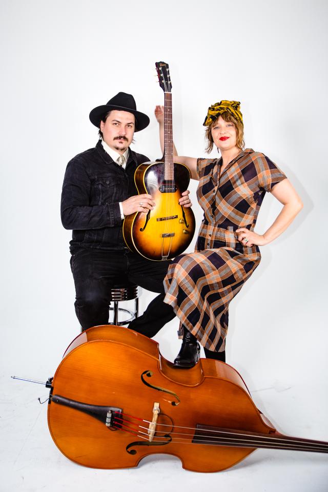 The two members of the band Blue Moon Marque pose with string instruments in front of a white background. The photo was taken by Wendy Wei and provided by the band.
