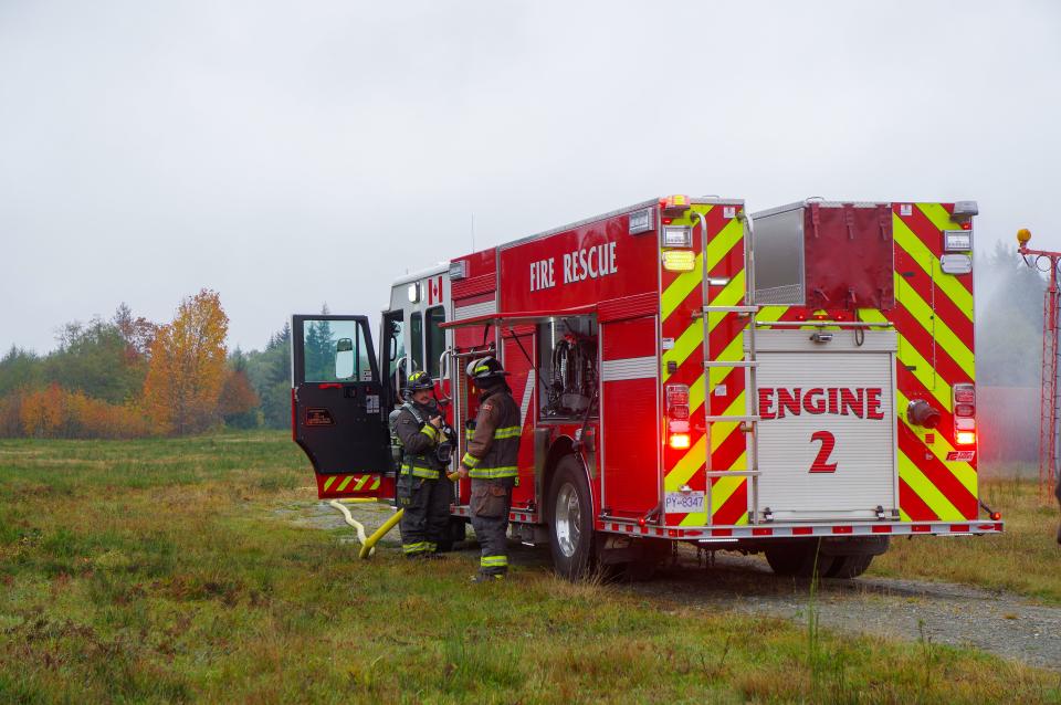 A fire truck named Engine 2 and two firefighters get things ready on the side of the truck. The front door is left open.