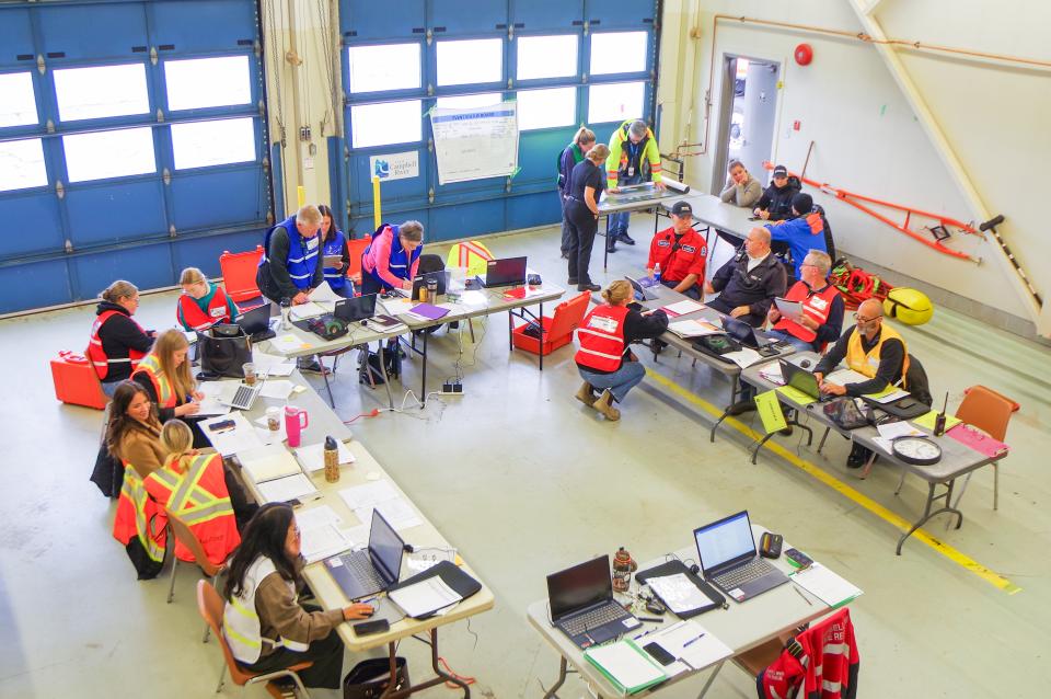 Tables in a rectangle formation with people in EOC vests gather together with computers and papers.