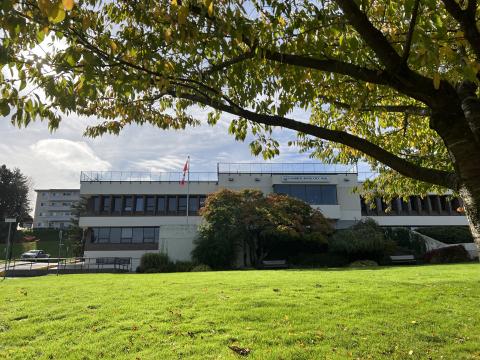 Exterior view of Campbell River's City Hall building. A Canada flag flies in front of the building. Greenery, a lawn and a leafy tree are in the foreground.