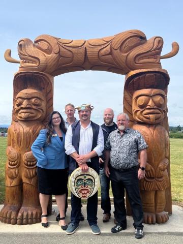 Mayor Dahl, City Council members and Chief Roberts in front of a carved Indigenous archway at ʔuxstalis (Tyee Spit).