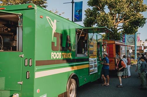 Bright green food truck with people lined up and being served food.