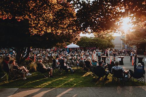 People sitting in lawn chairs and dancing under shaded areas on a sunny summer evening, enjoying live music performances at Campbell River's CR Live Streets Music in the Night event.