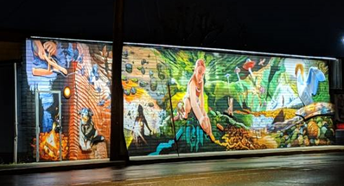 Illuminated mural on Shoppers Row featuring a child drawing with chalk and surrounded by vibrant, colorful images